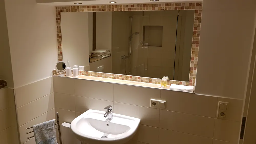 Helles Bad mit großem Spiegel, Waschbecken und Glasdusche.