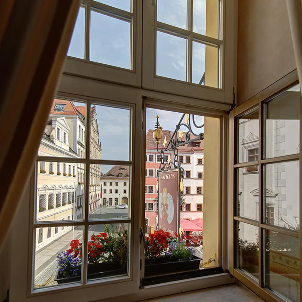 Blick aus einem geöffneten Fenster des Hotels auf den Untermarkt mit bunten Bürgerhäusern und dem Hotelschild.