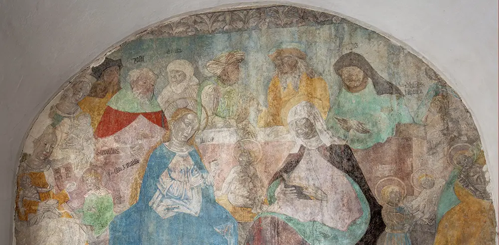 Wandmalerei im Bogenfeld: eine Gruppe heiliger Frauen und Männer, in der Mitte eine Frau mit Kind in blauem Mantel.