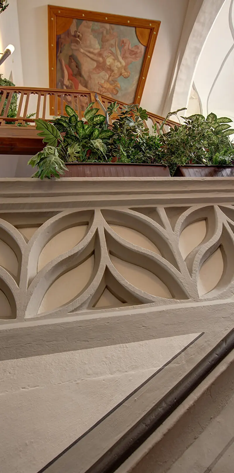 Steinerne Maßwerkbrüstung mit Fischblasen-Ornament, darüber Pflanzen und ein barockes Gemälde.