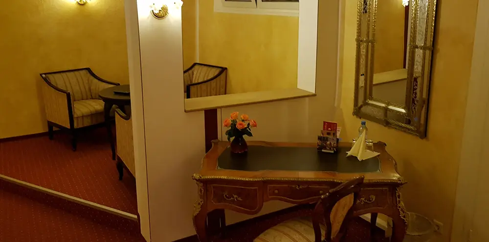 Vorraum eines Appartements mit Sesseln, einem antiken Sekretär mit Blumen und einem großen Spiegel.