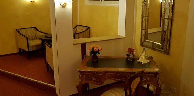 Vorraum eines Appartements mit Sesseln, einem antiken Sekretär mit Blumen und einem großen Spiegel.