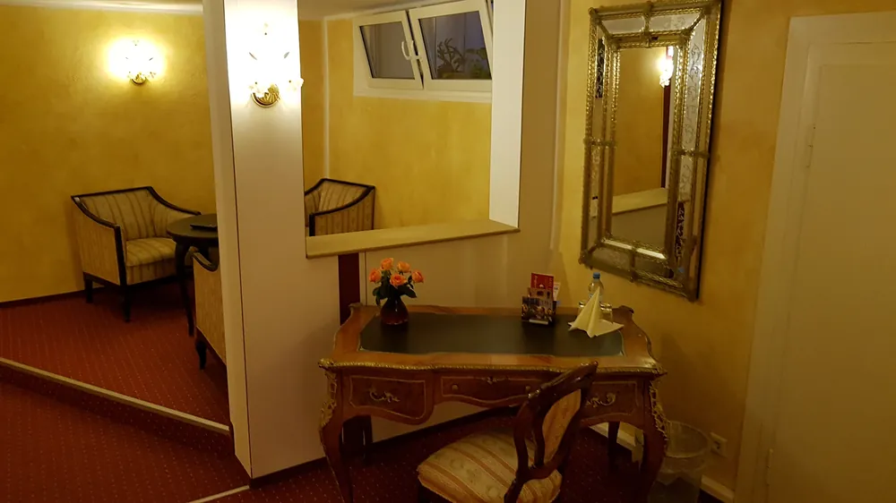 Sitzecke mit gepolsterten Sesseln, Spiegel und antikem Tischchen mit Blumen vor einem Fenster.